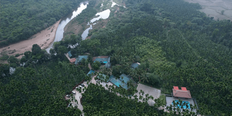 Aerial view showcasing a resort nestled by a serene river, surrounded by lush greenery and scenic landscapes.