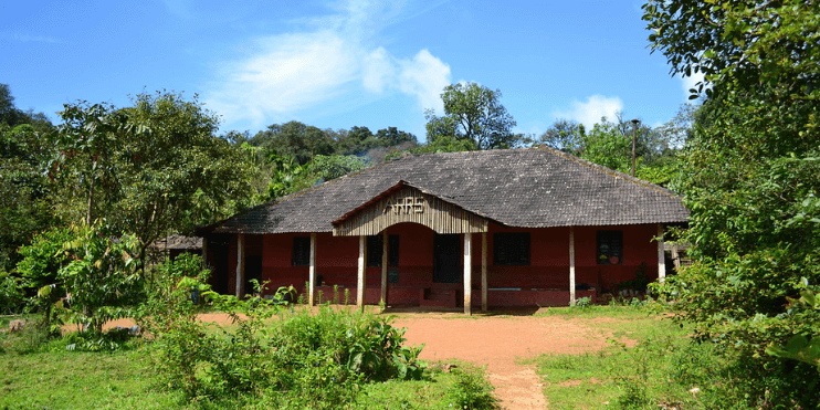 A traditional house with a thatched roof, set against the lush backdrop of the Agumbe Rainforest Research Station.