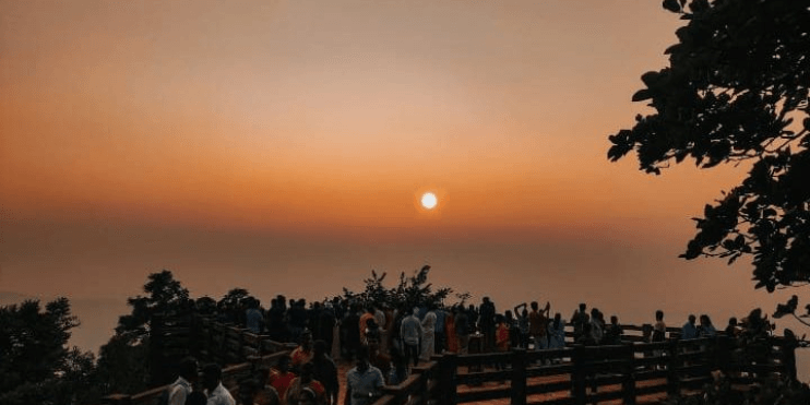 People standing on a wooden bridge at Agumbe Sunset Point, admiring the golden hues of the sunset over the Western Ghats.