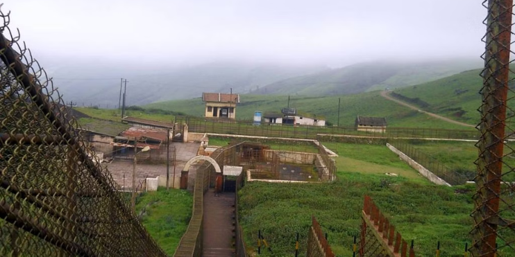 A scenic view of a fence and a building situated on a hill, surrounded by lush greenery under a clear sky.