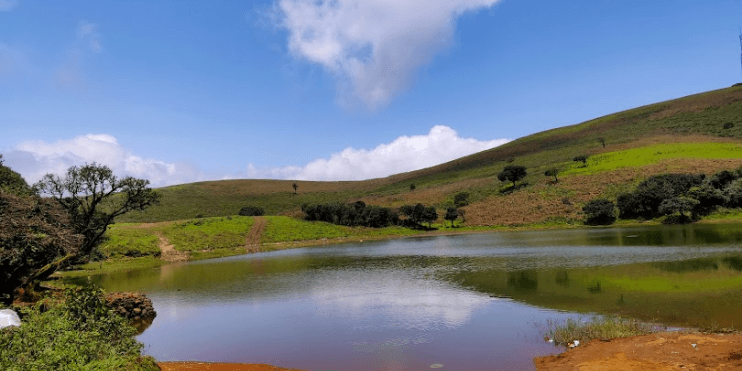 A tranquil lake surrounded by lush green hills and trees, reflecting the serene beauty of nature.