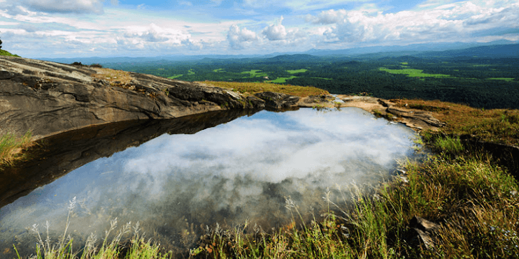 A serene mountain pool surrounded by grass and clouds, set atop Kundadri Hills, ideal for trekking and meditation.