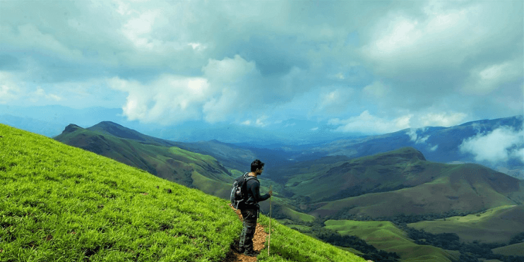 A man stands atop a hill, gazing at the majestic mountains, embodying the spirit of adventure in the Western Ghats.