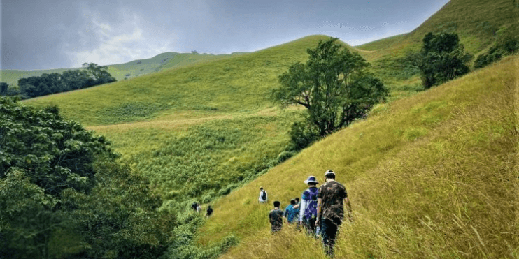 People walking up a grassy hill during the Kallusanka Trek, an adventure destination for outdoor enthusiasts.