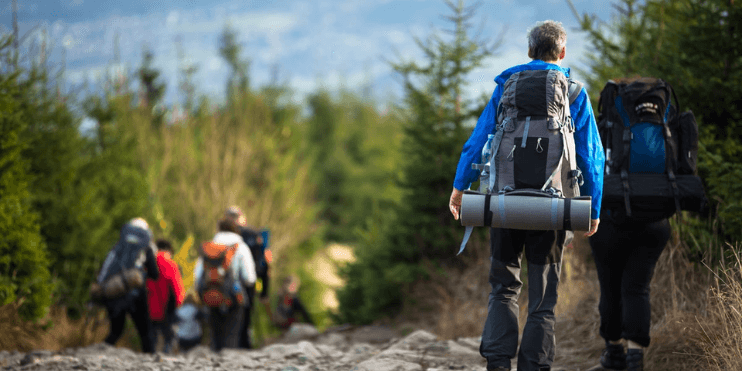 A group of hikers with backpacks descends a scenic trail, ready for their summer trekking adventure.