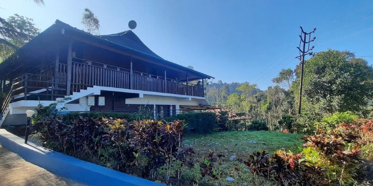 A house with a balcony surrounded by trees, set in a serene landscape ideal for a monsoon retreat in Chikmagalur.