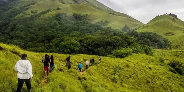 A group of hikers ascending Agni Gudda Hill, surrounded by lush greenery and panoramic valley views.