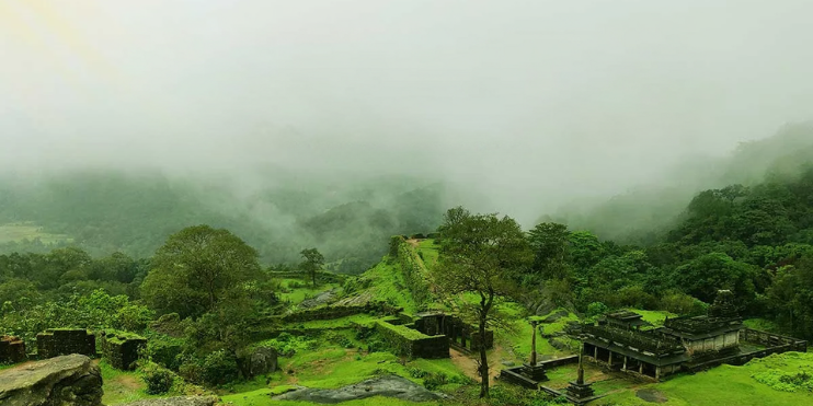 Lush green valley with a stone building, showcasing the serene beauty of Agumbe's monsoon landscape in Karnataka.