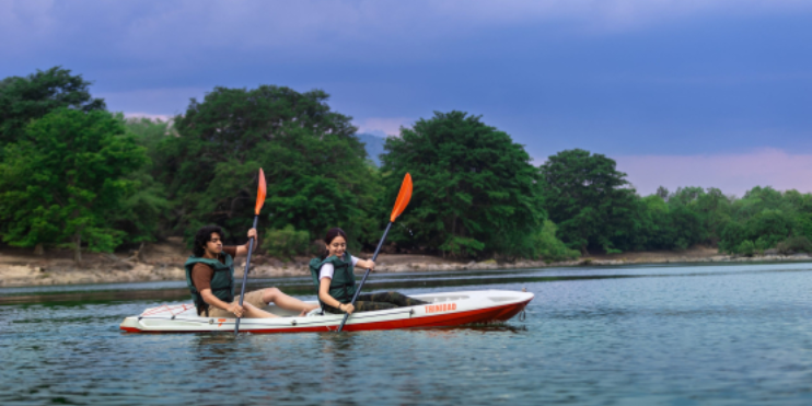 Two people kayaking on a serene lake surrounded by lush greenery at Bheemeshwari, a popular adventure destination near Bangalore.