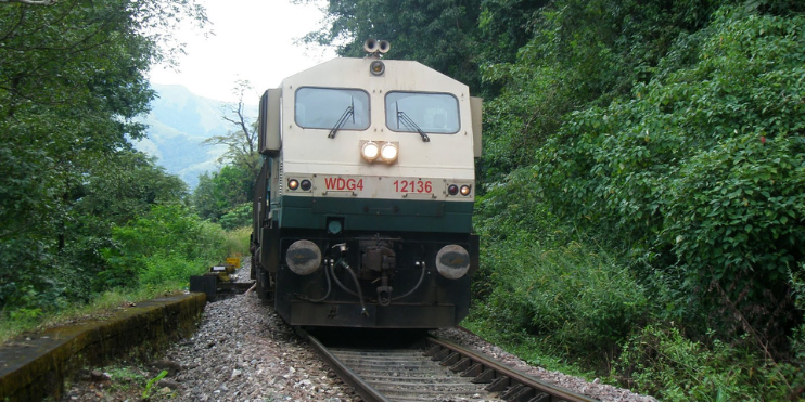 A train travels along tracks through a lush forest, showcasing the scenic beauty of the Ghats in Sakleshpur.