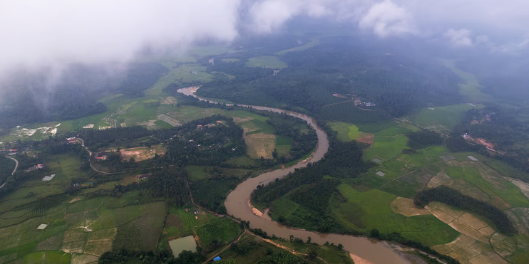 Aerial view of a winding river surrounded by lush farmland and mountains, showcasing the scenic beauty of the region.