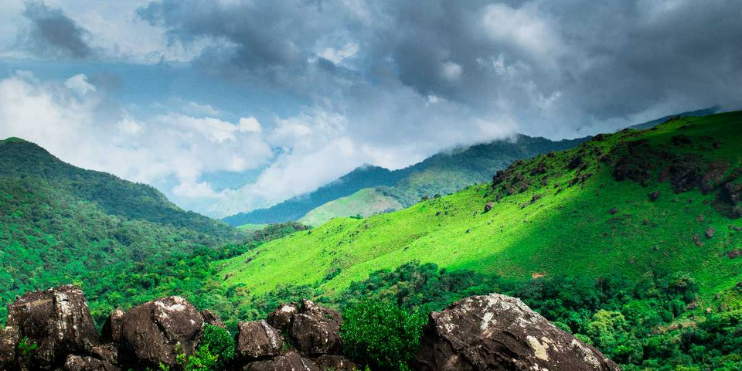A scenic view of green mountain ranges with rocks and trees, representing the natural beauty of Coorg, India.