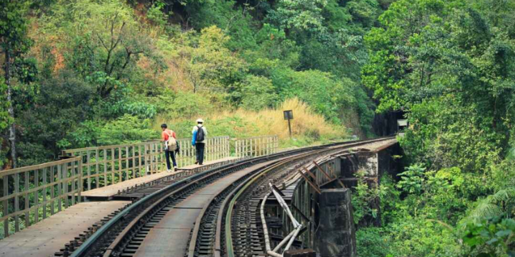 Two people walking along train tracks on a scenic railway bridge trek in Sakleshpur, surrounded by natural beauty.