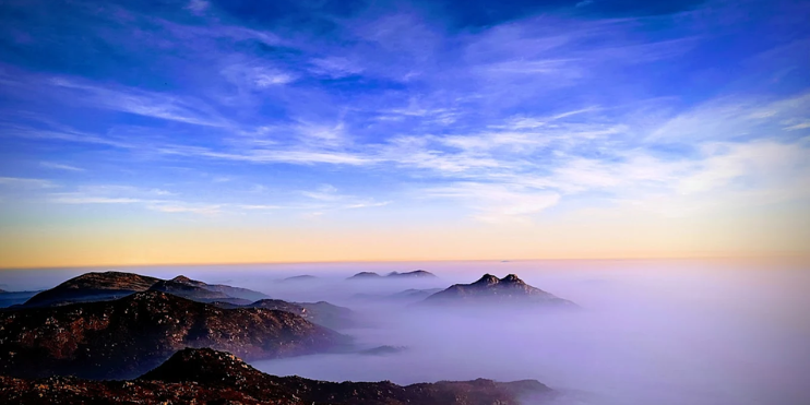 People stand atop Skandagiri mountain, gazing at a sea of clouds during a breathtaking sunrise trek.