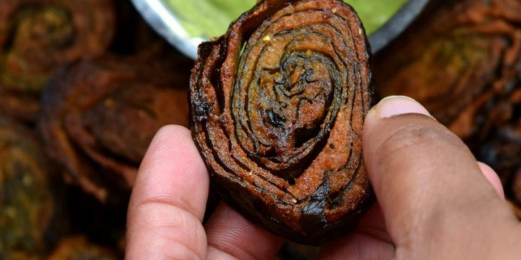 A person holds a piece of food drizzled with green sauce, showcasing a traditional Malnad dish.